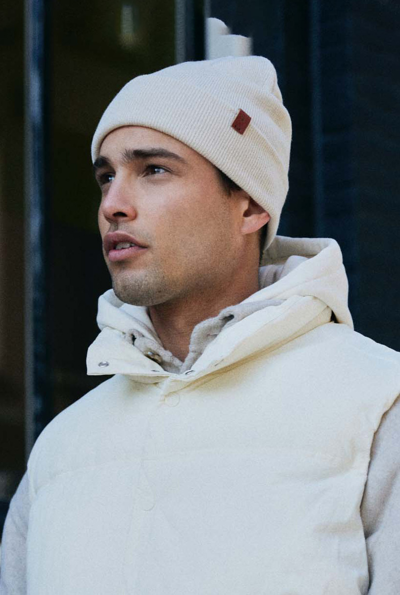 man wearing beanie from bickley and mitchell in pastel colours with a building in Amsterdam as the background
